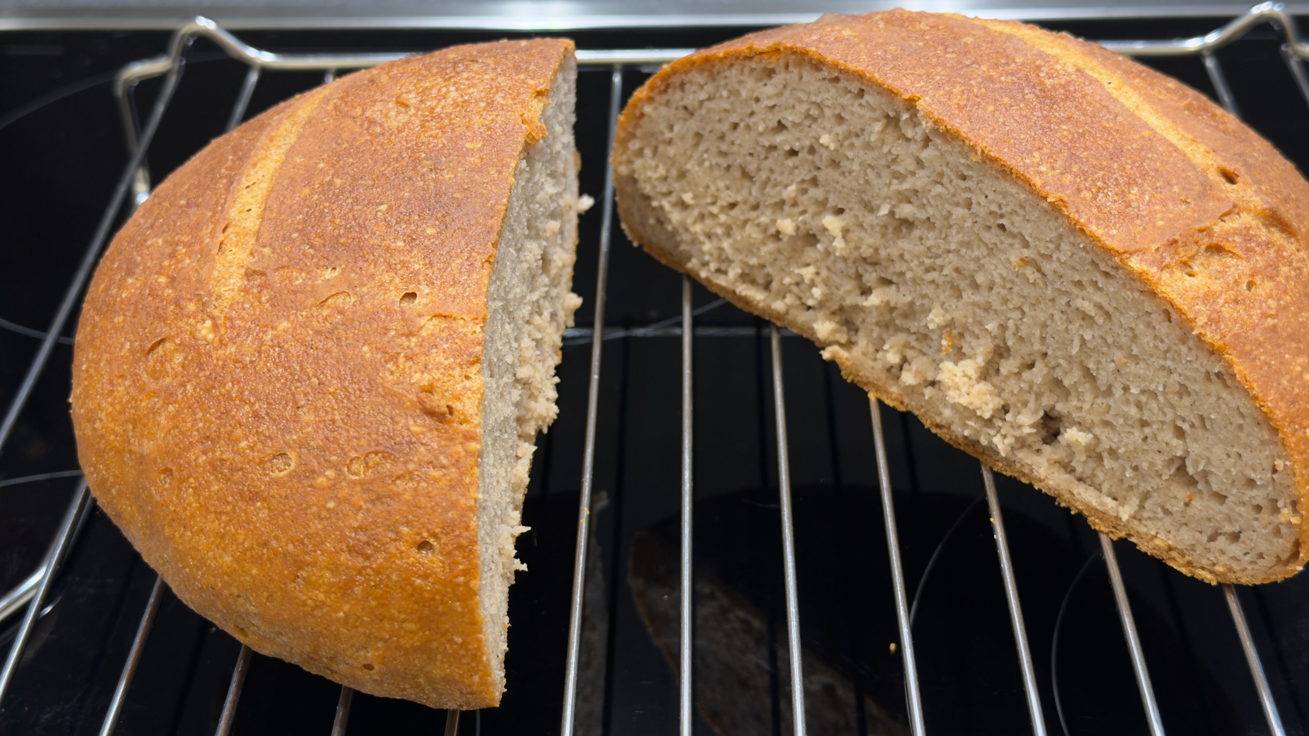 A freshly baked loaf of bread, cut in half to reveal its soft interior, resting on a wire rack.